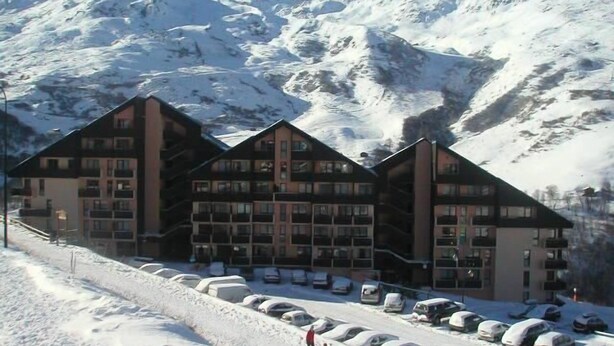 Un hôtel à plusieurs étages, un parking et, en arrière-plan, des montagnes enneigées.