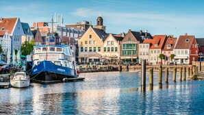 A waterfront with colorful buildings, a docked boat, and wooden pilings. - Ferienwohnung direkt am Deich in St.Peter-Ording (St. Peter-Ording)