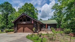 Une cabane en rondins avec un garage, entourée d’un jardin et d’arbres.