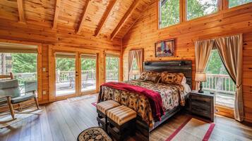 A wooden cabin bedroom with a large bed, a rocking chair, and a view of the outdoors.