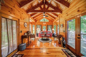Una cabaña de madera espaciosa con techo alto, una zona de estar central con un sofá rojo y grandes ventanas con vistas al exterior.