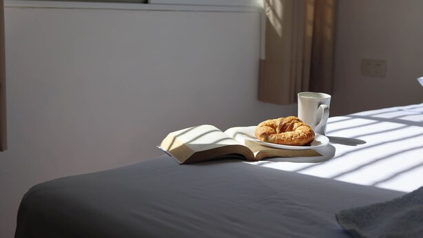 A bed with a book and a croissant on a plate, and a cup beside it. - Apartamento 22 (Bacalar)