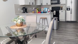 Una cocina moderna con armarios blancos, una mesa de comedor de vidrio y un refrigerador de acero inoxidable.