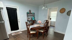 Un coin repas avec une table et des chaises en bois, une cuisine équipée d’un réfrigérateur et une porte avec un rideau noir.