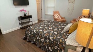 Une chambre à coucher comprenant un lit, un bureau, une chaise, une télévision, un ventilateur de plafond et un attrape-rêves.