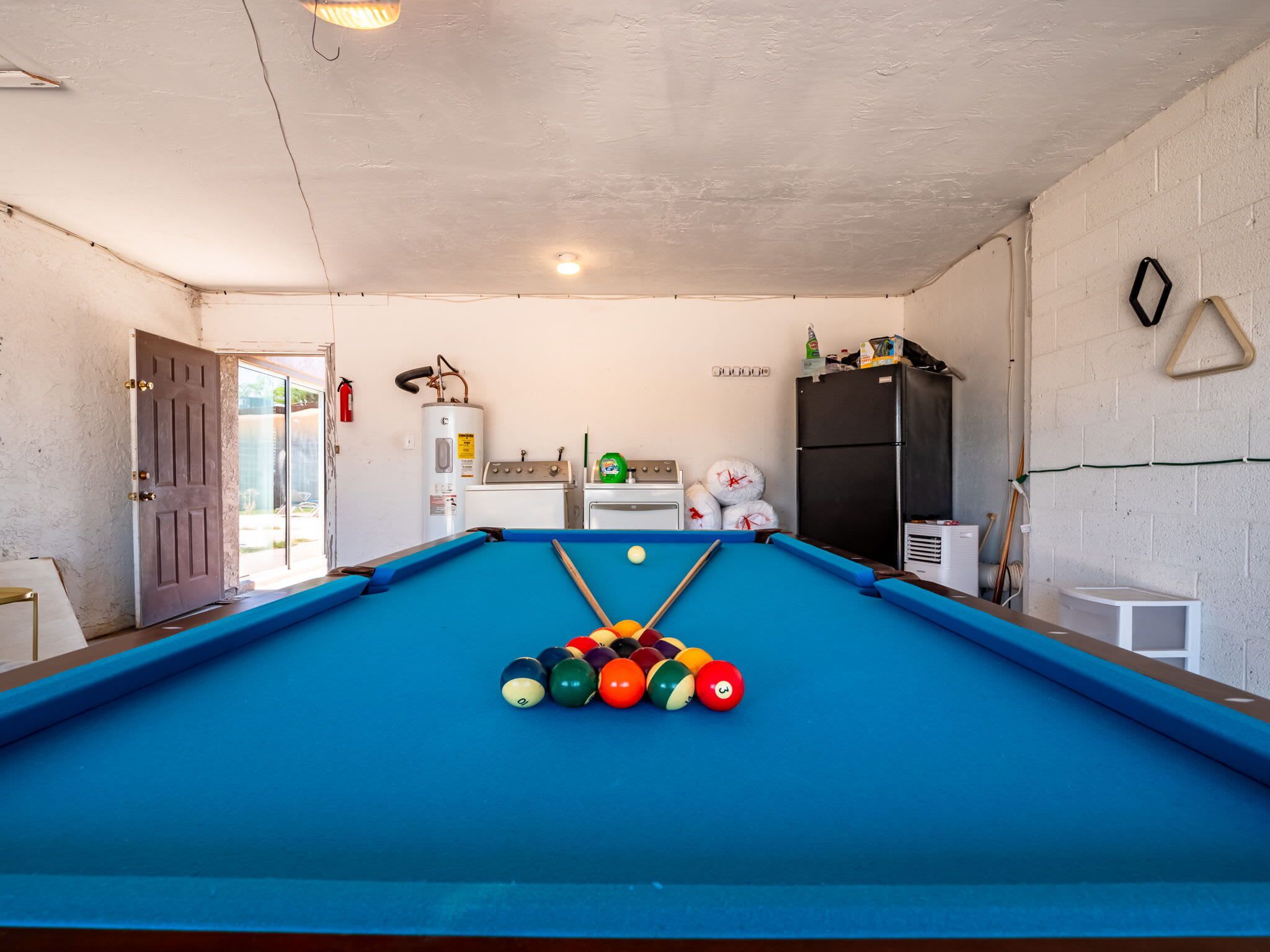 A pool table with balls, a water heater, a stove, and a refrigerator in a room with a white brick wall.