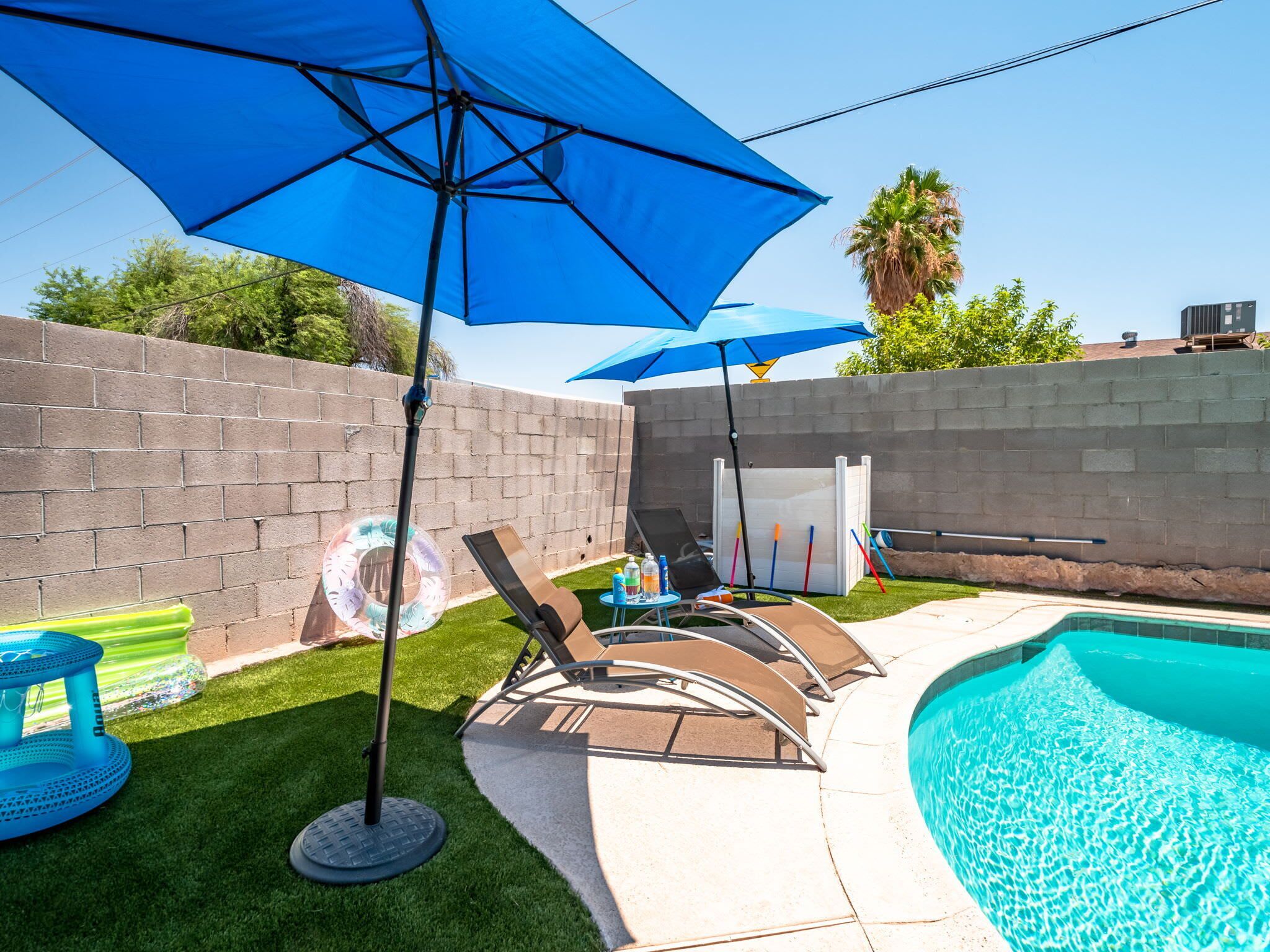 A backyard with a swimming pool, lounge chairs, and umbrellas.