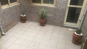 A tiled patio area with three potted plants and a window. - Royale Crown Villa Apartment (Abuja)