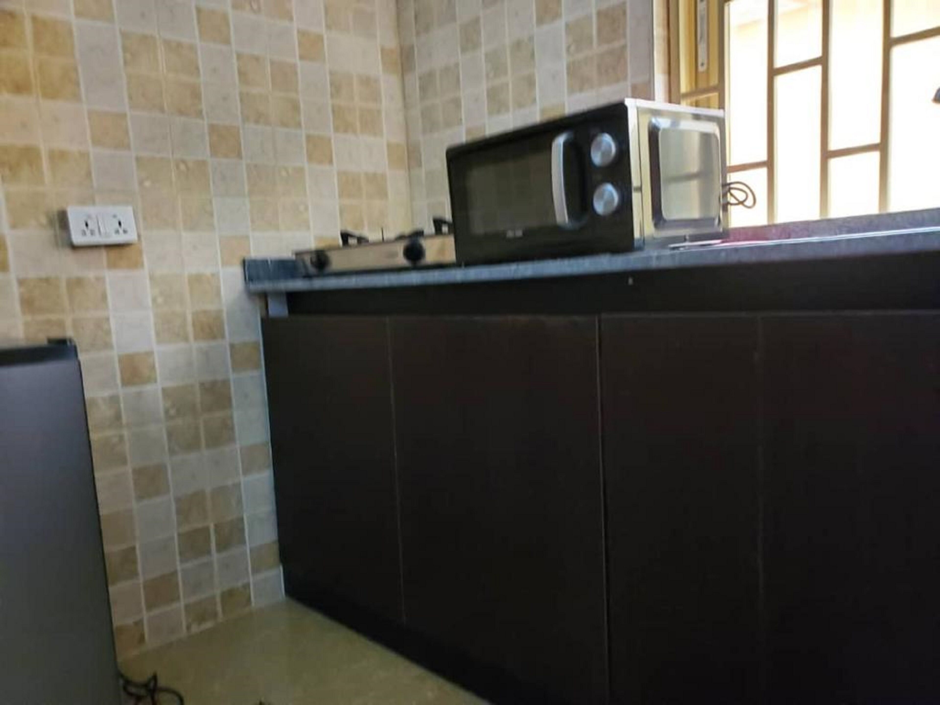 A kitchen with a microwave on the counter, a tiled backsplash, and a window with bars.