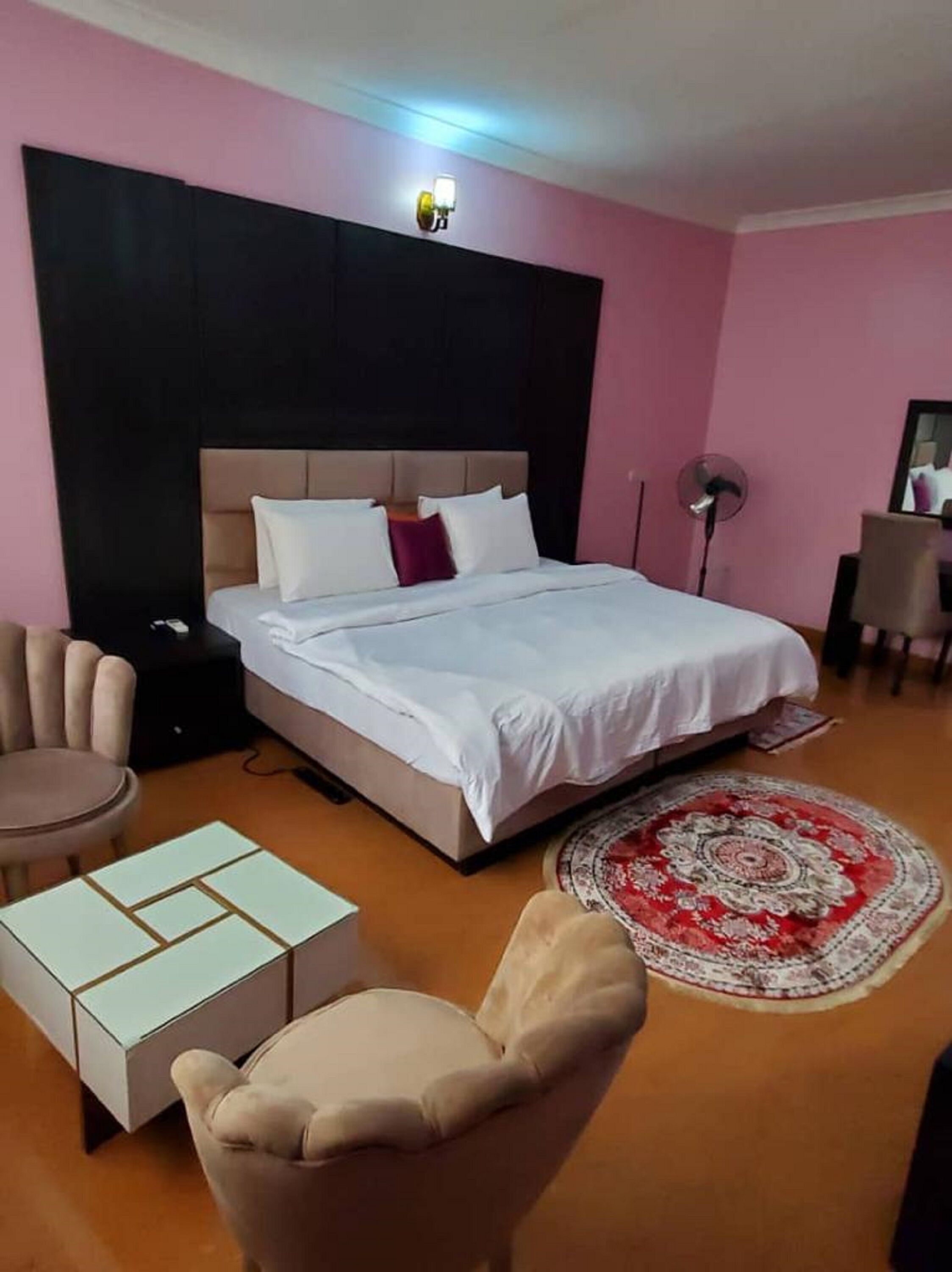 A hotel room with a bed, a chair, a small table, and a floor lamp.