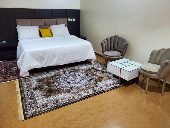 A bedroom with a bed, two chairs, a small table, and a patterned rug.