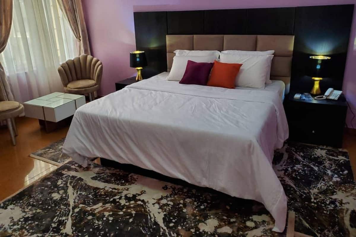 Een hotelkamer met een groot bed, een stoel, een nachtkastje en een lamp.