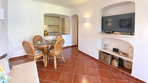 Un ambiente compatto con angolo ristoro, cucina e televisore a parete.