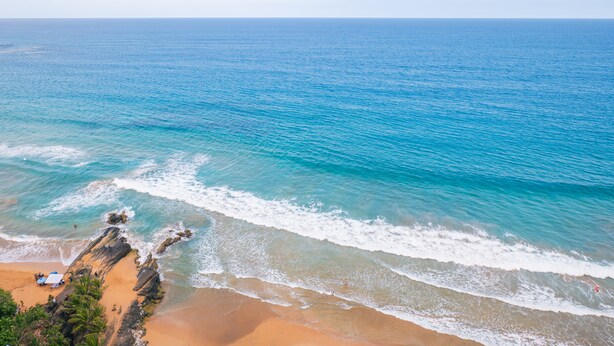 Ein Strand mit klarem, blauem Wasser, Sandstrand und Felsen.