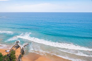 A beach with clear blue water, sandy shore, and rocky outcrops. - A cozy apartment with a spectacular ocean view! (Luquillo)