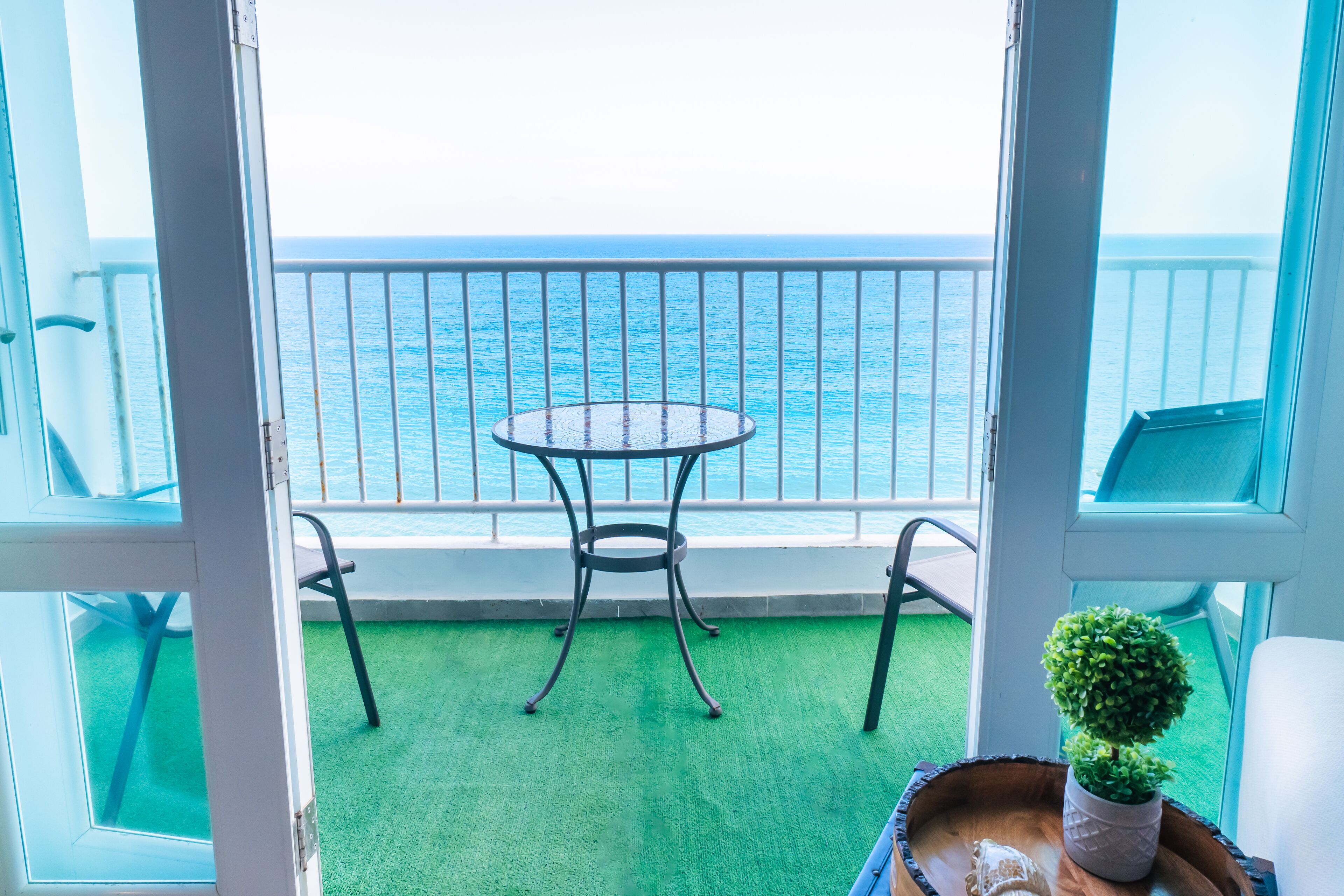 Een balkon met een tafel en stoelen, een kleine potplant en uitzicht op de zee.