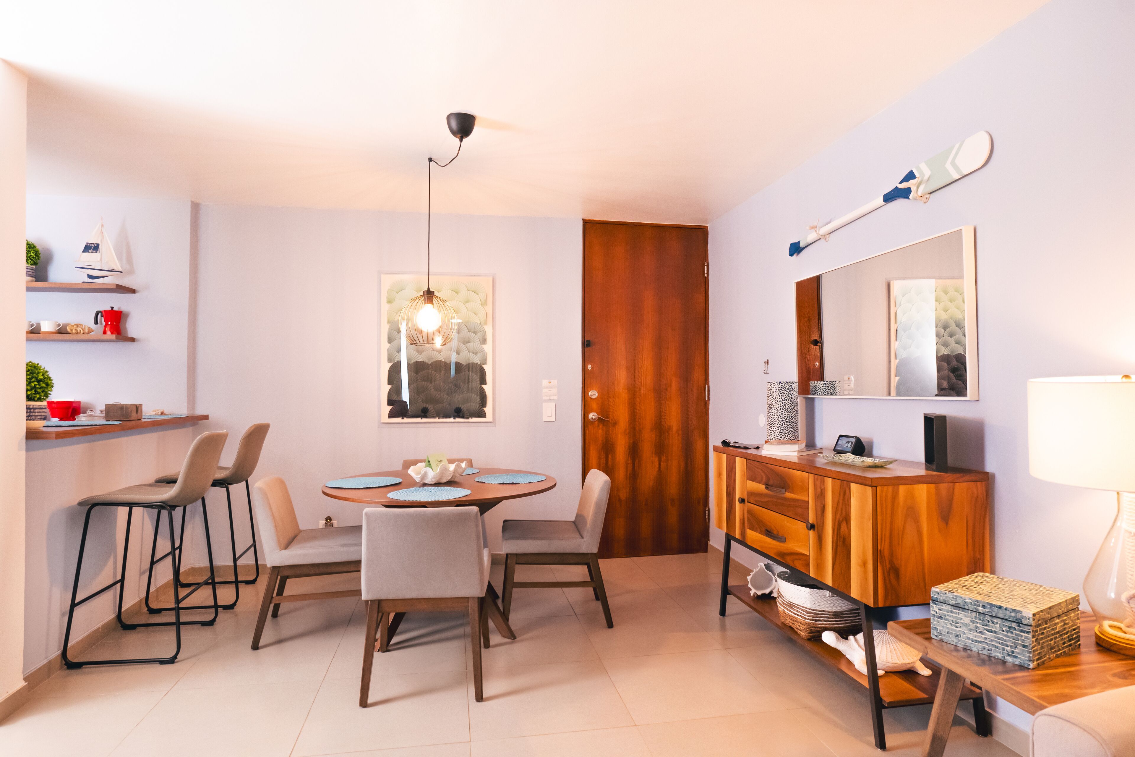 Uma sala de jantar moderna com uma mesa redonda, quatro cadeiras, um armário de madeira e um espelho sobre o armário.