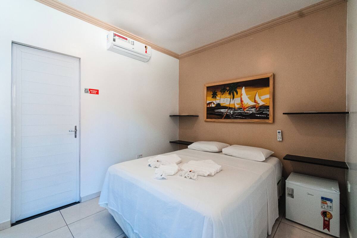 Quarto de hotel com cama, um quadro, mini-frigorífico e porta.
