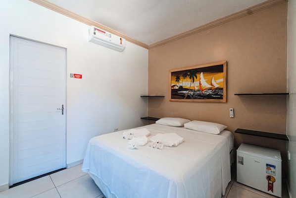 Habitación de hotel con una cama, un cuadro, un refrigerador pequeño y una puerta.