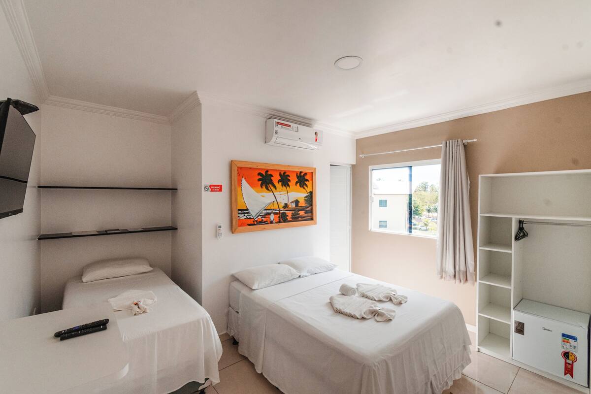 Quarto de hotel com duas camas, um quadro, ar condicionado, janela com cortinas e um guarda-roupa.