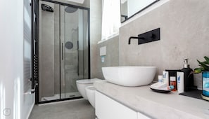 A modern bathroom with a glass shower enclosure, a white sink, and a toilet.