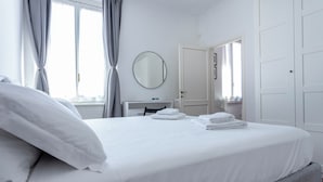 A hotel room with a neatly made bed, a round mirror on the wall, a radiator, and a door leading to another room. - Italianway - Cristoforo Colombo 5B (Milan)