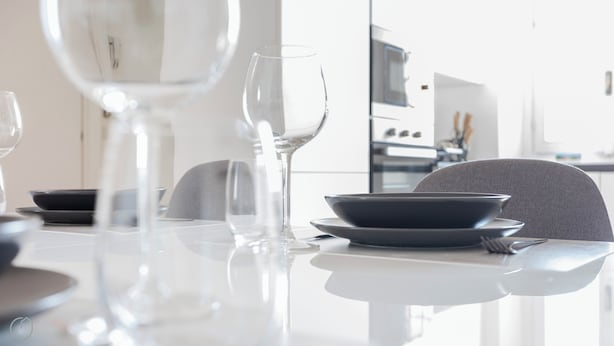 A modern dining table with clear glassware and dark plates, set in a bright kitchen area with a neutral color scheme. - Italianway - Cristoforo Colombo 5B (Milan)