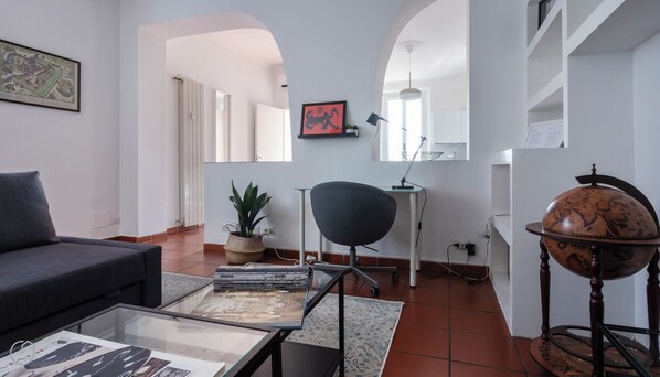A living room with a sofa, a glass coffee table with magazines, a chair, a globe, and a map on the wall.