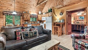 Un accogliente interno di una baita con un divano in pelle, un tavolo da pranzo in legno e un angolo cottura con pensili in legno e un frigorifero.