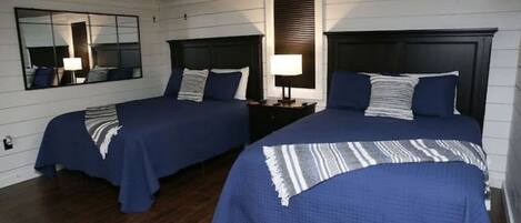 A room with two beds, wooden flooring, a large mirror, and a ceiling fan.