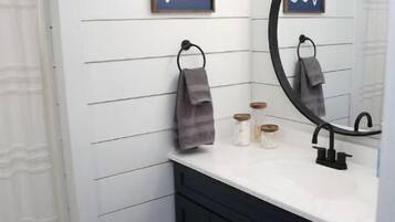 Un baño con paredes blancas, un mueble de tocador oscuro, un espejo redondo y un perchero para toallas.