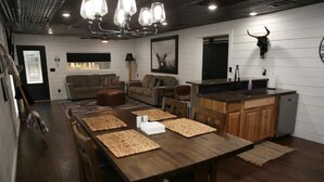 A spacious living area with a wooden dining table, sofas, and a kitchen area with a bull skull decoration. - Hidden Gem Cottages (Palestine)