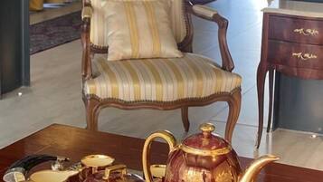 A room with a striped armchair, a side table with a lamp, and a tray with teapots and a sugar bowl.