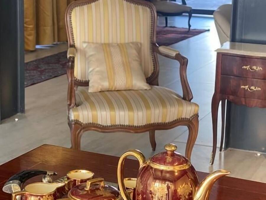 A room with a striped armchair, a side table with a lamp, and a tray with teapots and a sugar bowl.