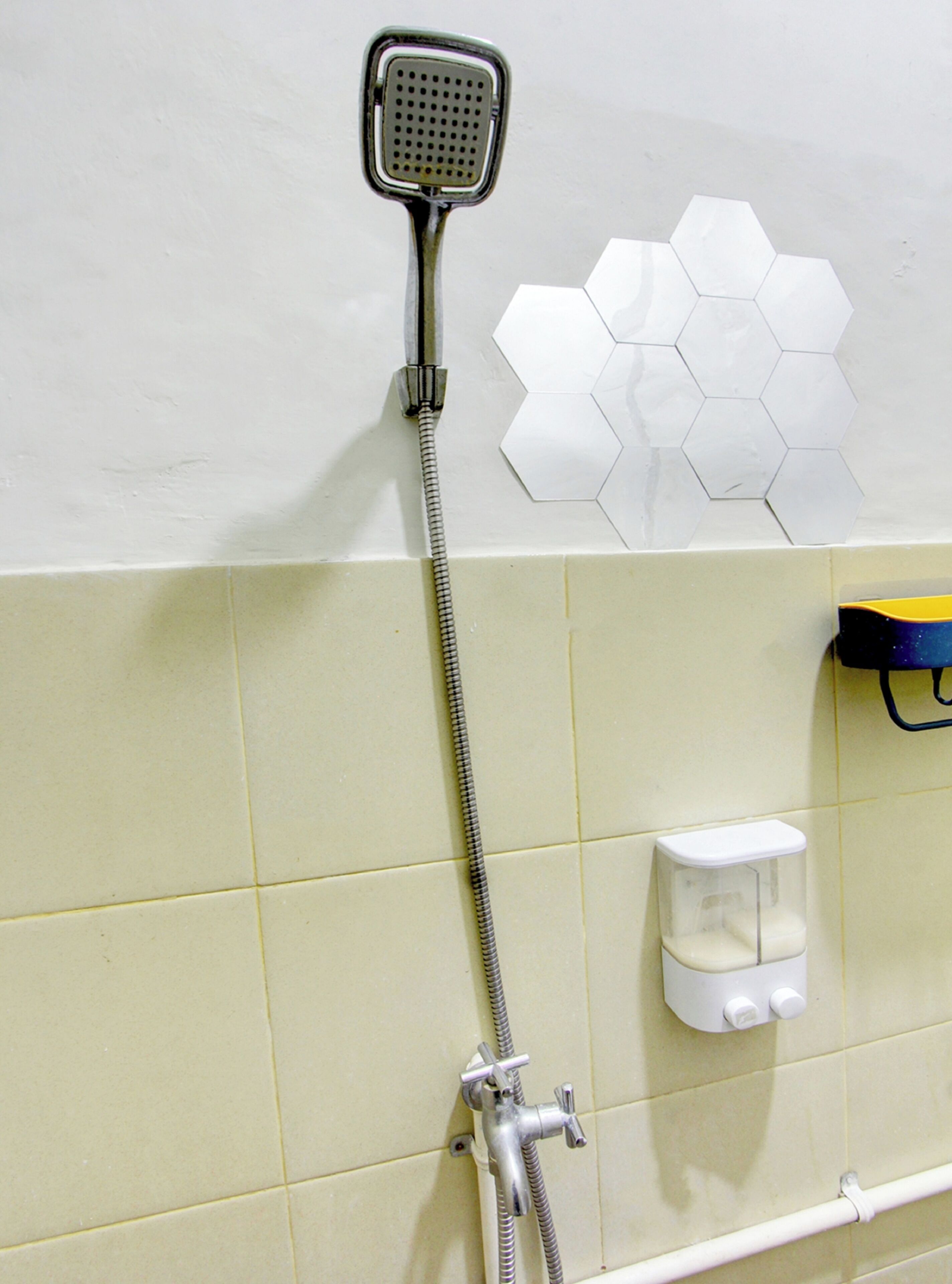A shower with a handheld showerhead and a wall-mounted faucet. There is a soap dispenser on the wall.