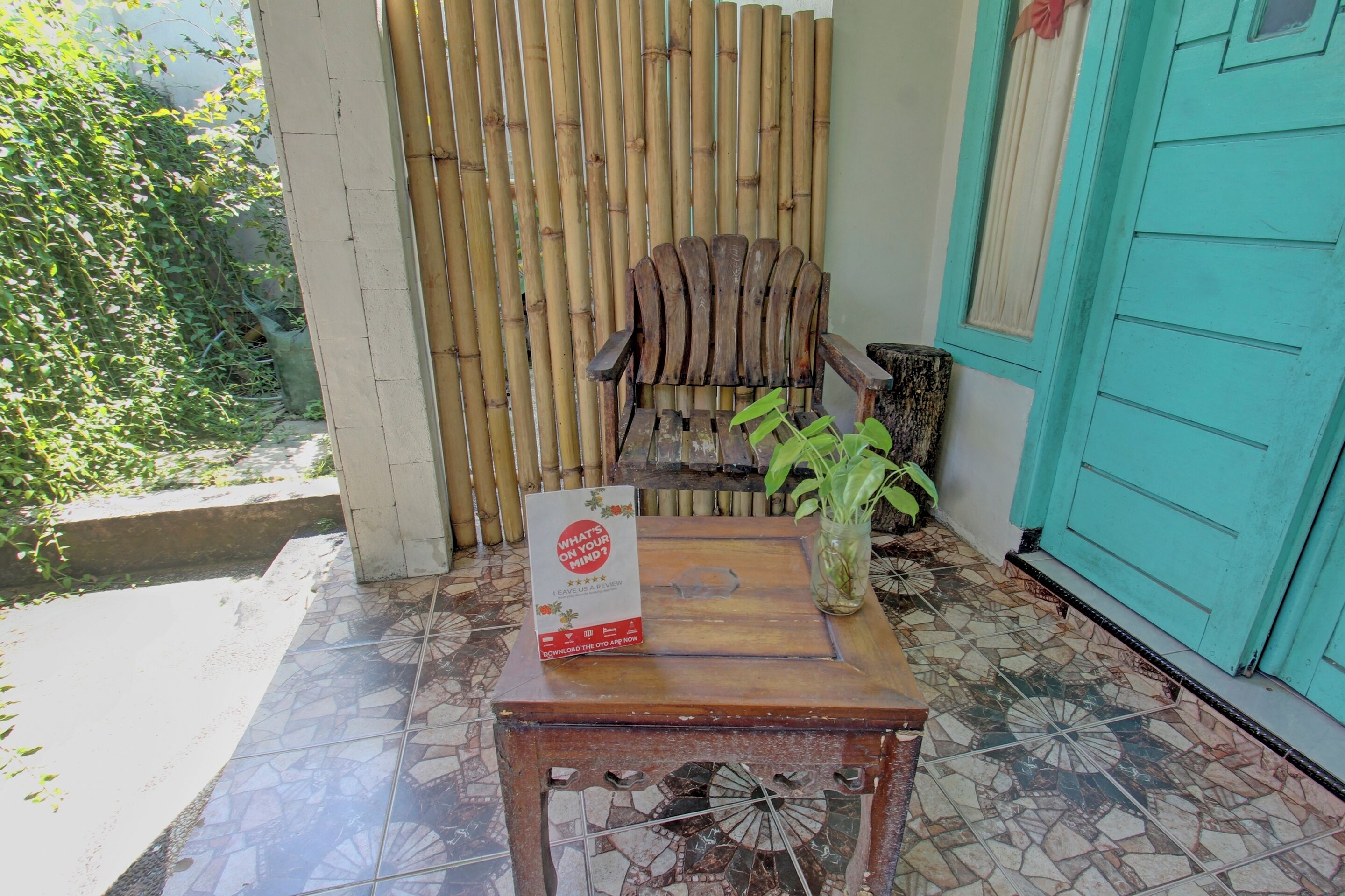 A wooden table with a sign, a chair, and a potted plant on a tiled patio.