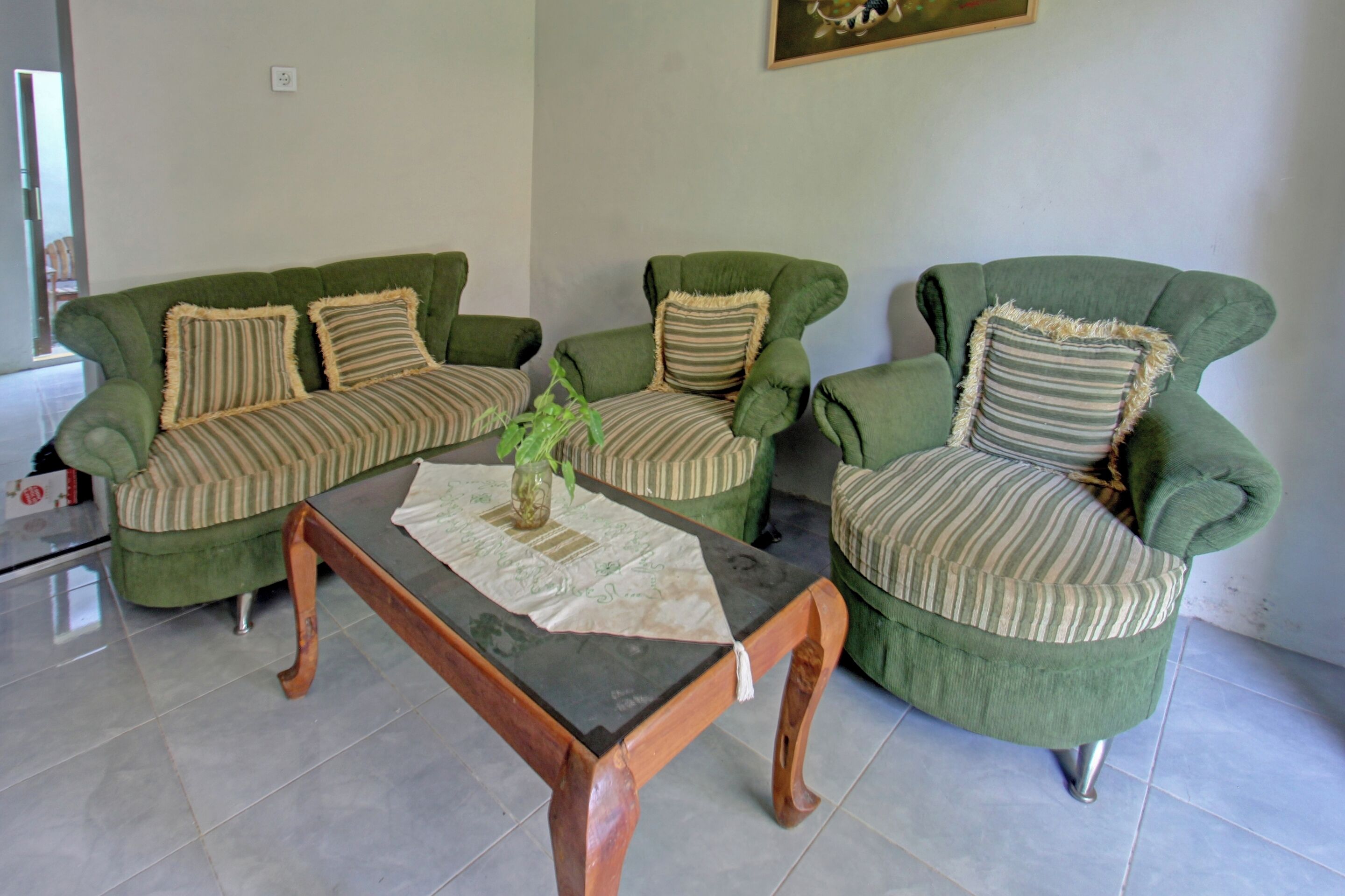 A living room with a green sofa set, striped cushions, and a wooden coffee table with a vase.