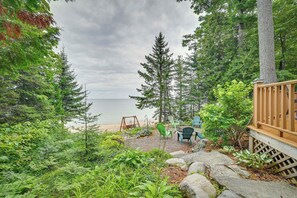 A wooden deck with a swing set, chairs, and a view of the beach and ocean.