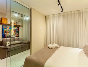 Habitación de hotel con cama, sofá, separador de vidrio y un cuadro en la pared.