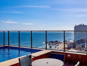 Un balcón con piscina, sillas y vista al océano y la playa.