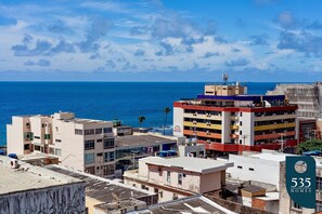 Un paisaje urbano costero con un edificio destacado que tiene una terraza en la azotea y varios balcones.