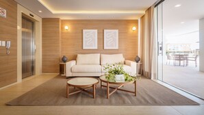 Een moderne woonkamer met een bank, twee bijzettafeltjes en een plant. Rechts is een schuifdeur van glas, en links een aan de muur bevestigd toestel.