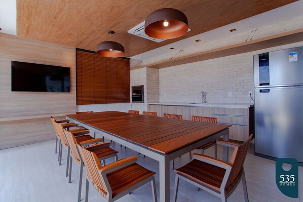 A modern kitchen with a large wooden table and chairs, a built-in oven, and a stainless steel refrigerator.