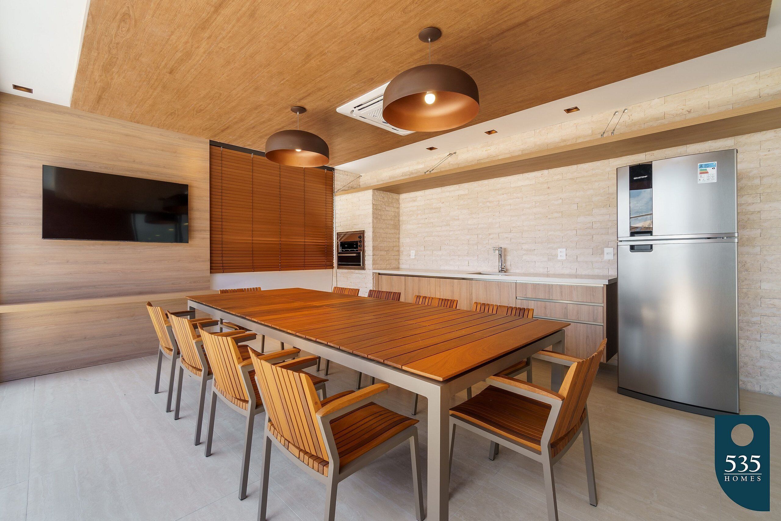 A modern kitchen with a large wooden table, built-in appliances, and pendant lighting.