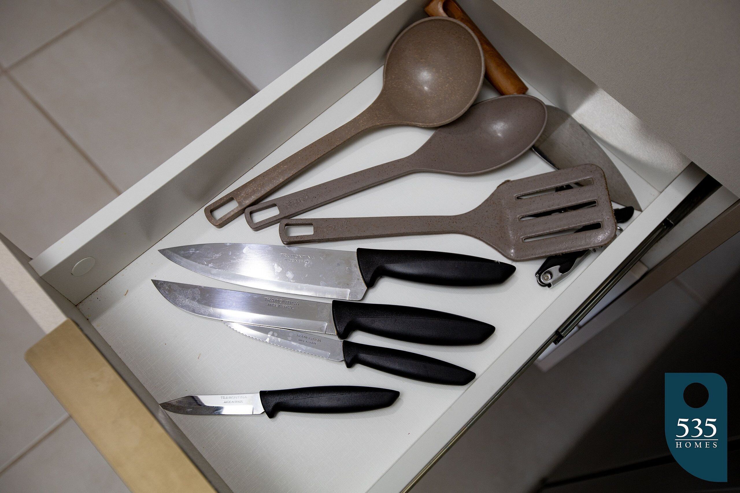 A drawer containing various kitchen utensils including a spoon, spatula, and knives.