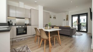 Una cocina moderna con electrodomésticos integrados, una zona de comedor con sillas de madera y un sofá gris.