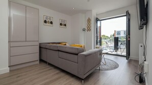Una sala moderna con un sofá gris, una pequeña mesa redonda y vistas al exterior a través de una puerta de vidrio.