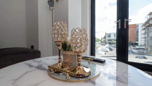 Una mesa de mármol con dos candelabros ornamentados, un control remoto y una planta pequeña.