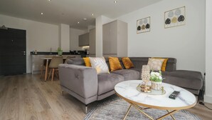 Una sala de estar moderna con un sofá gris, una mesa de centro redonda y un comedor con una mesa y sillas.