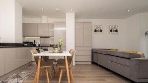 Una cocina moderna con zona de comedor, un sofá gris y dos cuadros con motivos de hojas en la pared.